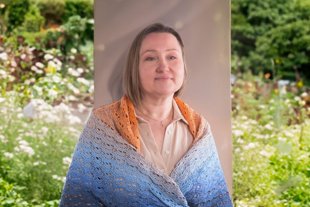 młoda kobieta otulona ażurową chustą w kolorach pomarańczowym i niebieskim